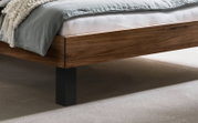 Detailfoto van een modern houten bed met een warm generfd bedrandje en een zwart metalen onderstel, met grijs beddengoed en een wit matras, gezien vanuit een zijdelingse hoek van onderaf