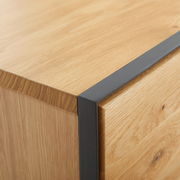 Nahaufnahme einer Ecke eines Möbelstücks aus Holz mit schwarzem Metallakzent, perspektivisch von oben betrachtet.