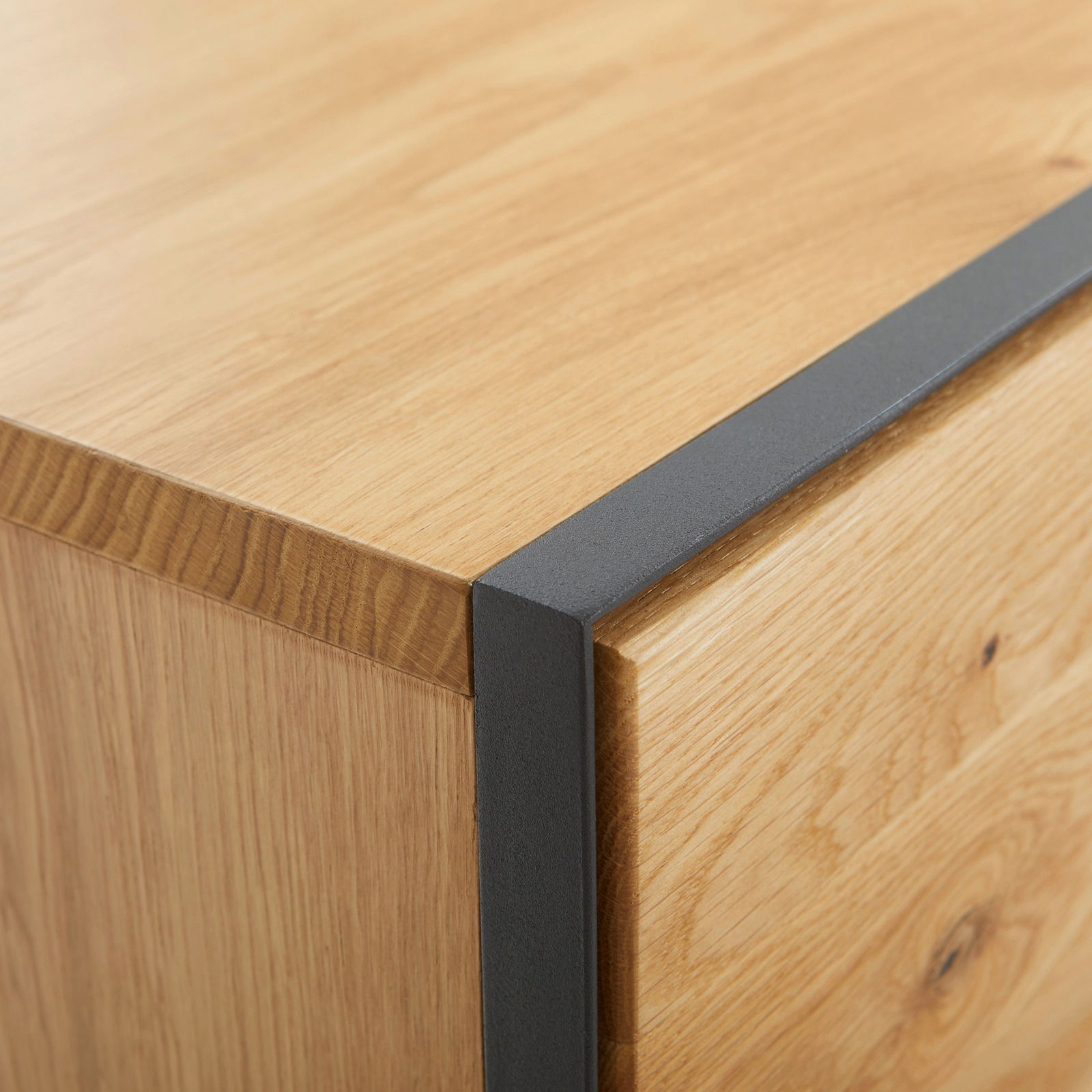 Nahaufnahme einer Ecke eines Möbelstücks aus Holz mit schwarzem Metallakzent, perspektivisch von oben betrachtet.