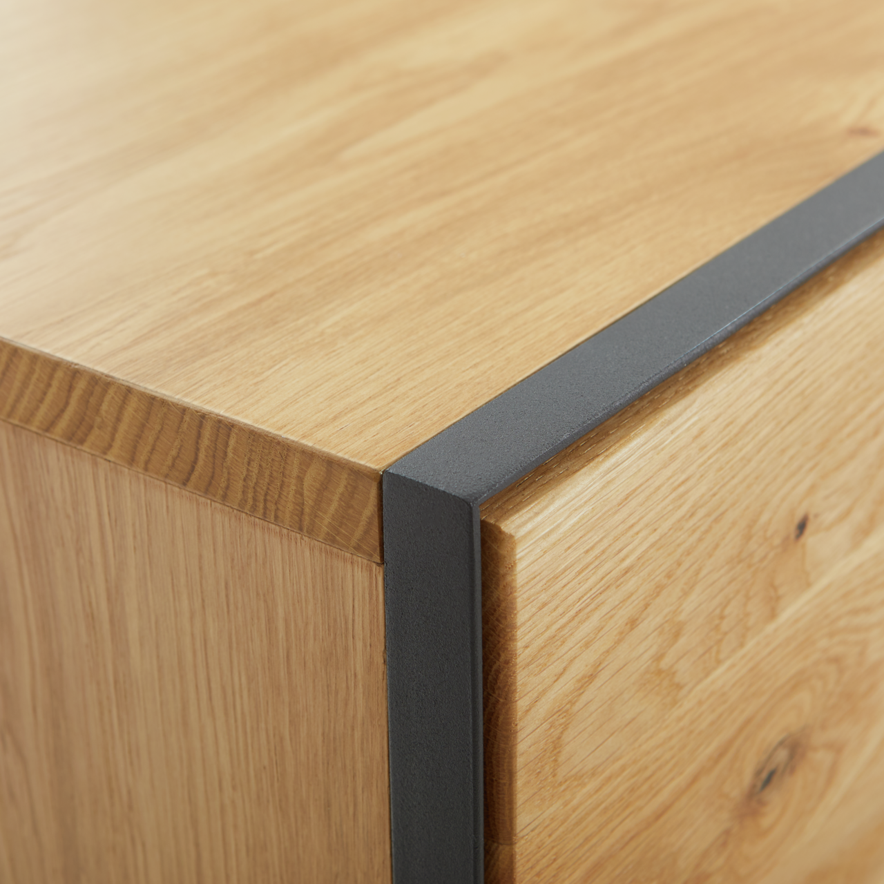 Nahaufnahme einer Ecke eines Möbelstücks aus Holz mit schwarzem Metallakzent, perspektivisch von oben betrachtet.