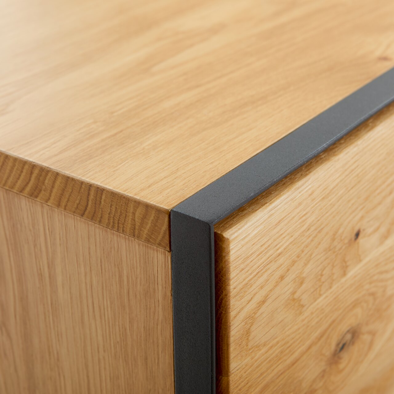 Nahaufnahme einer Ecke eines Möbelstücks aus Holz mit schwarzem Metallakzent, perspektivisch von oben betrachtet.