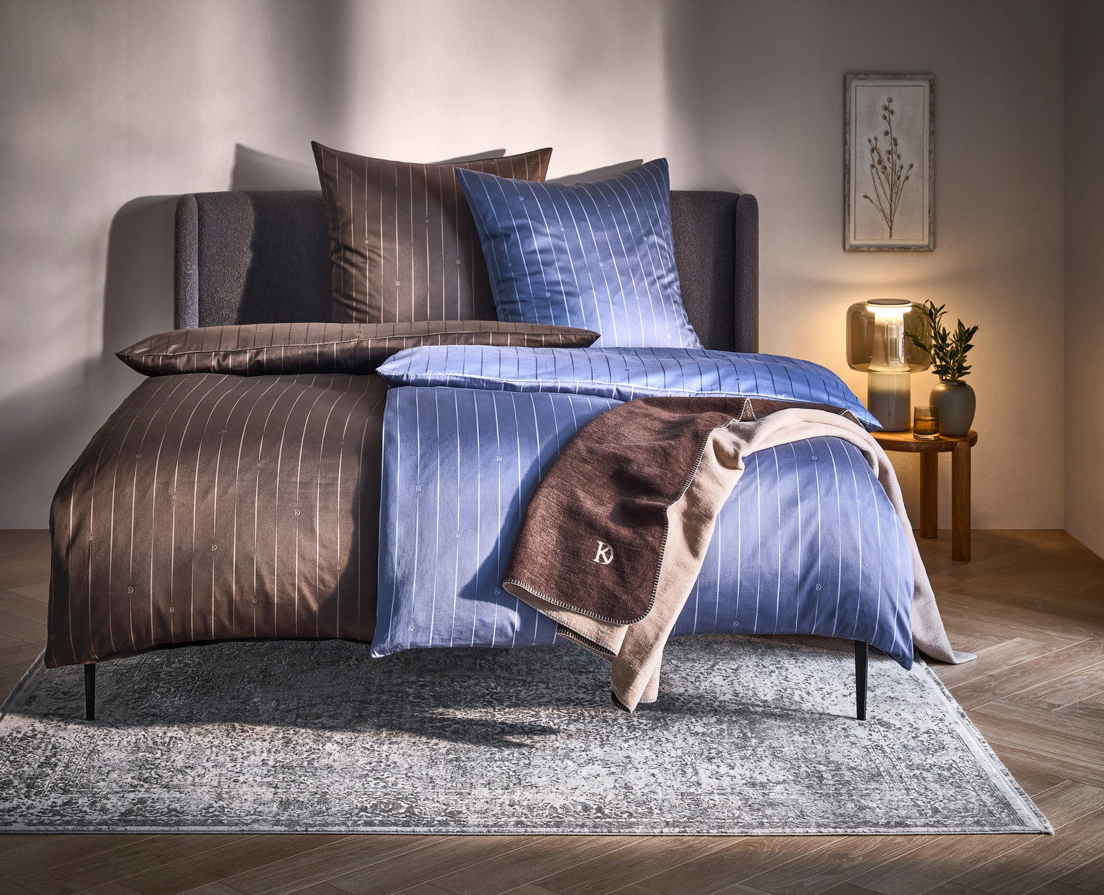 Dieter Knoll Omkeerbaar beddengoed Wendebettwäsche in Braun und Blau mit feinen Streifen, auf einem Bett in einem gemütlich eingerichteten Schlafzimmer, seitliche Perspektive.
