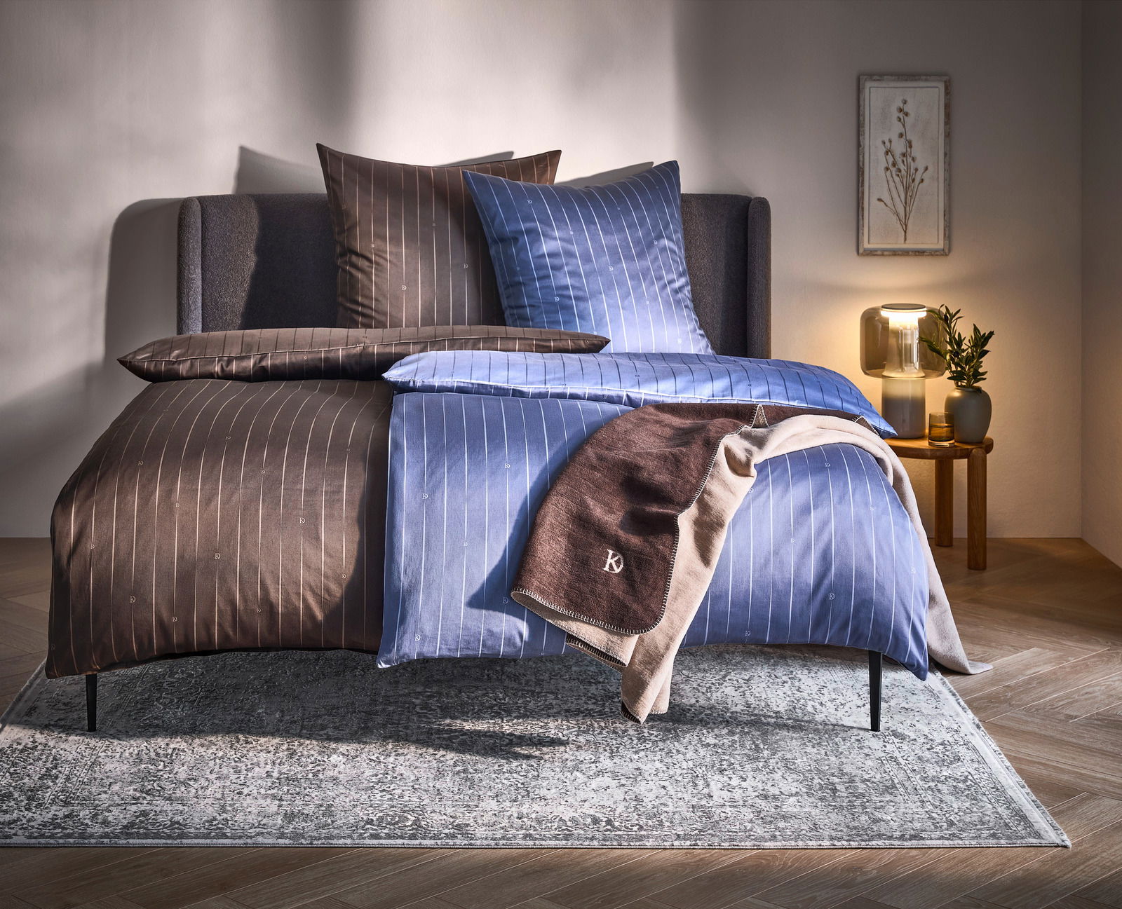 Wendebettwäsche in Braun und Blau mit feinen Streifen, auf einem Bett in einem gemütlich eingerichteten Schlafzimmer, seitliche Perspektive.