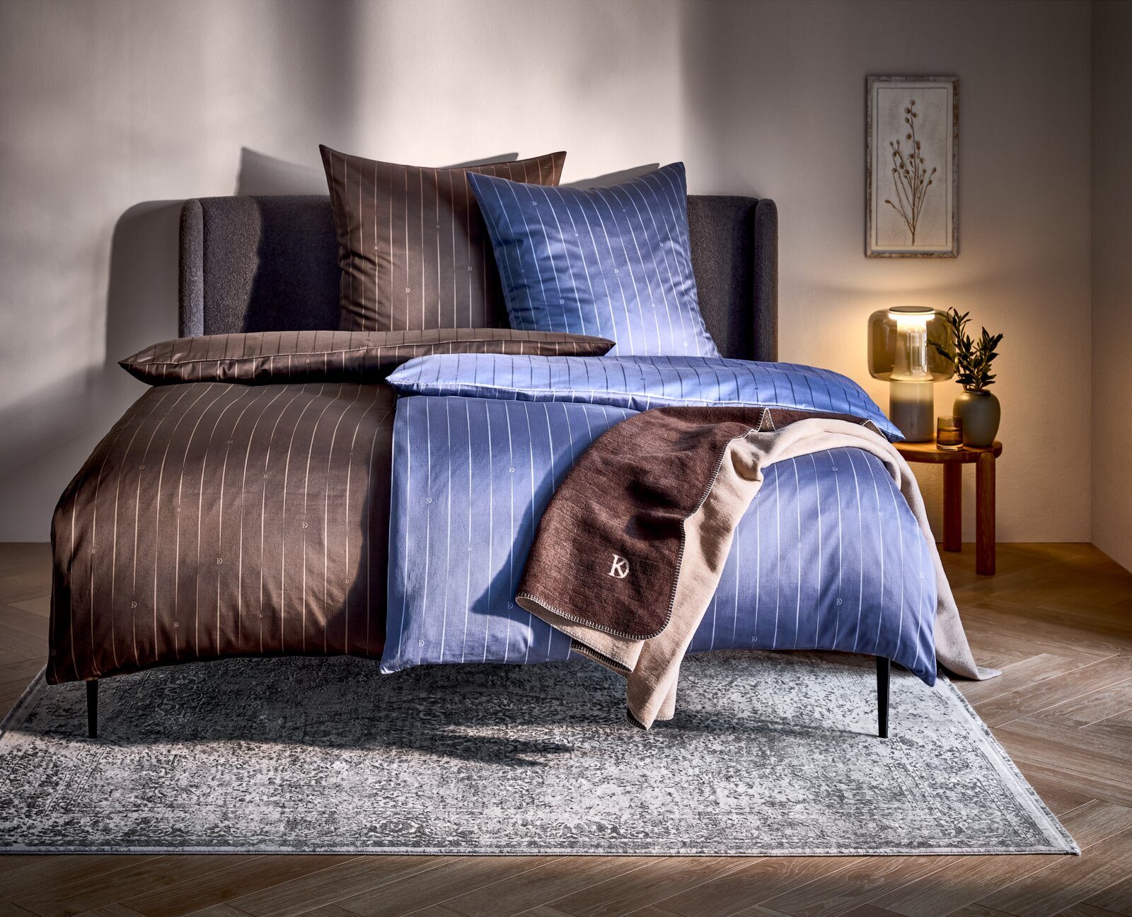 Dieter Knoll Satin Wendebettwäsche 135/200cm Wendebettwäsche in Braun und Blau mit feinen Streifen, auf einem Bett in einem gemütlich eingerichteten Schlafzimmer, seitliche Perspektive.