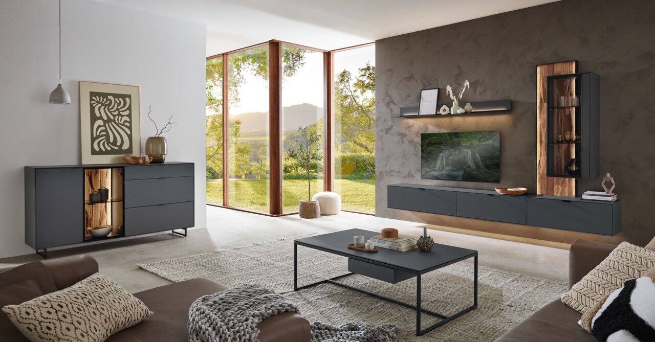 Moderne woonkamer met een wandplank in een donkere houttint, stijlvol ingericht, met uitzicht op grote ramen en een groen landschap.