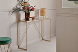 Elegante Konsole mit goldfarbenem Gestell und Glasplatte, dekoriert mit einer Vase und Lampe, seitliche Perspektive.