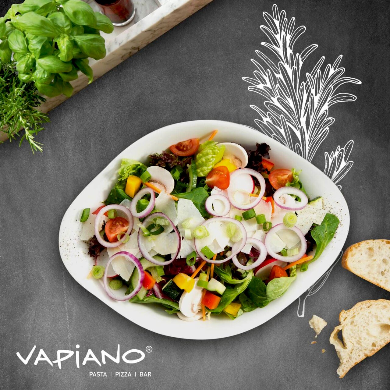 Frische Salatschüssel mit verschiedenen Gemüsesorten aus der Vogelperspektive, umgeben von Kräutern und Brot, auf einer Tafel mit Vapiano-Logo.