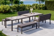 Lounge-Bank-Set auf einer Terrasse mit Blick auf einen Garten und das Meer, bestehend aus zwei Tischen, einer Bank und einer Sitzbank, gedeckt für ein Essen im Freien.