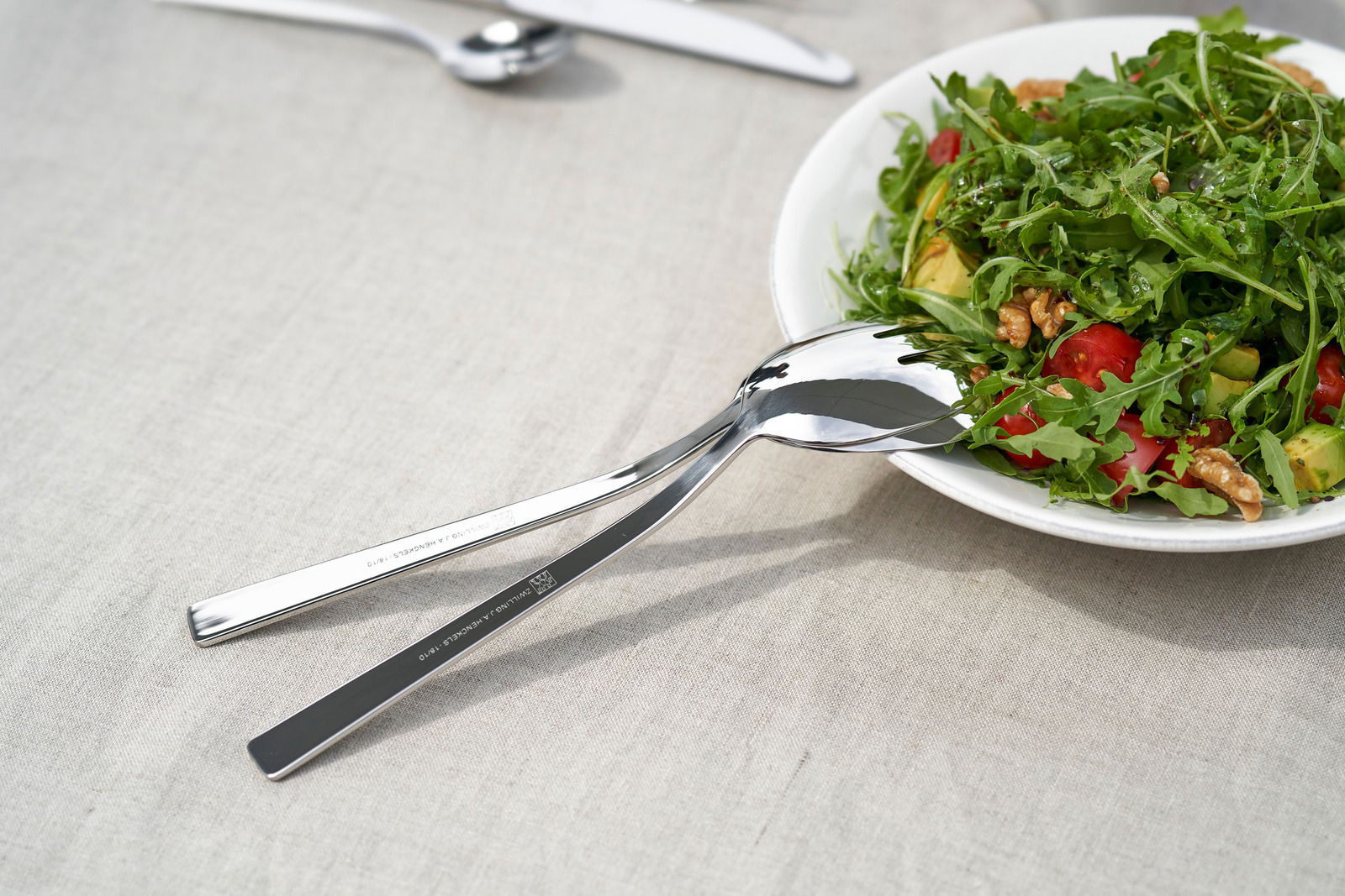 Nahaufnahme von glänzendem Besteck auf einem Tisch neben einem Salatteller, Perspektive von oben.