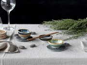 Schlicht gedeckter Tisch mit drei glasierten Keramikschälchen auf runden Schiefer-Untersetzern, Essstäbchen und Deko-Grün, fotografiert aus leicht erhöhter, schräger Seitenperspektive.