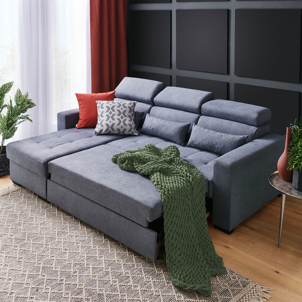 Ecksofa MONSON Graue Rundecke (L) mit verstellbaren Kopfstützen, dekoriert mit roten und gemusterten Kissen sowie einer grünen Decke, aus der Perspektive von vorne links.