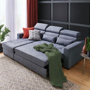 Graue Rundecke (L) mit verstellbaren Kopfstützen, dekoriert mit roten und gemusterten Kissen sowie einer grünen Decke, aus der Perspektive von vorne links.