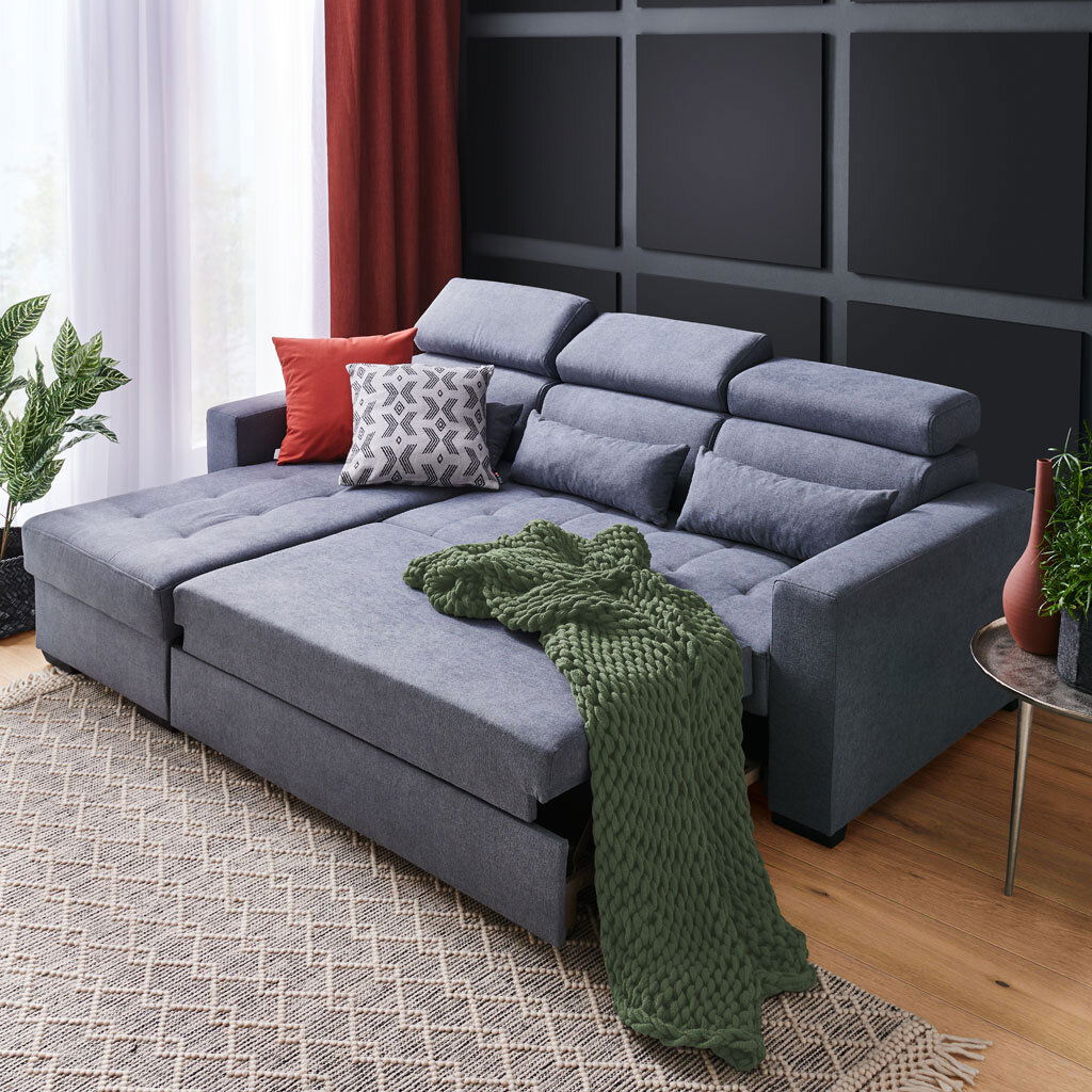 Ecksofa MONSON Graue Rundecke (L) mit verstellbaren Kopfstützen, dekoriert mit roten und gemusterten Kissen sowie einer grünen Decke, aus der Perspektive von vorne links.