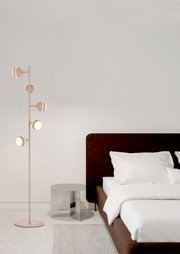 Moderne poederroze vloerlamp met vijf ronde lichtkoppen, vanuit schuin vooraanzicht naast een stijlvol bed weergegeven