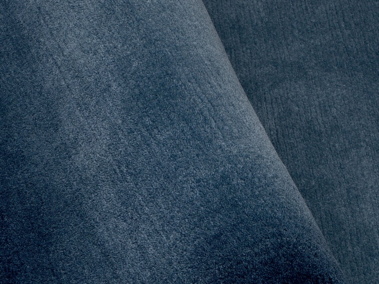 Nahaufnahme eines blauen Teppichs mit weicher Textur, perspektivisch von der Seite aufgenommen.