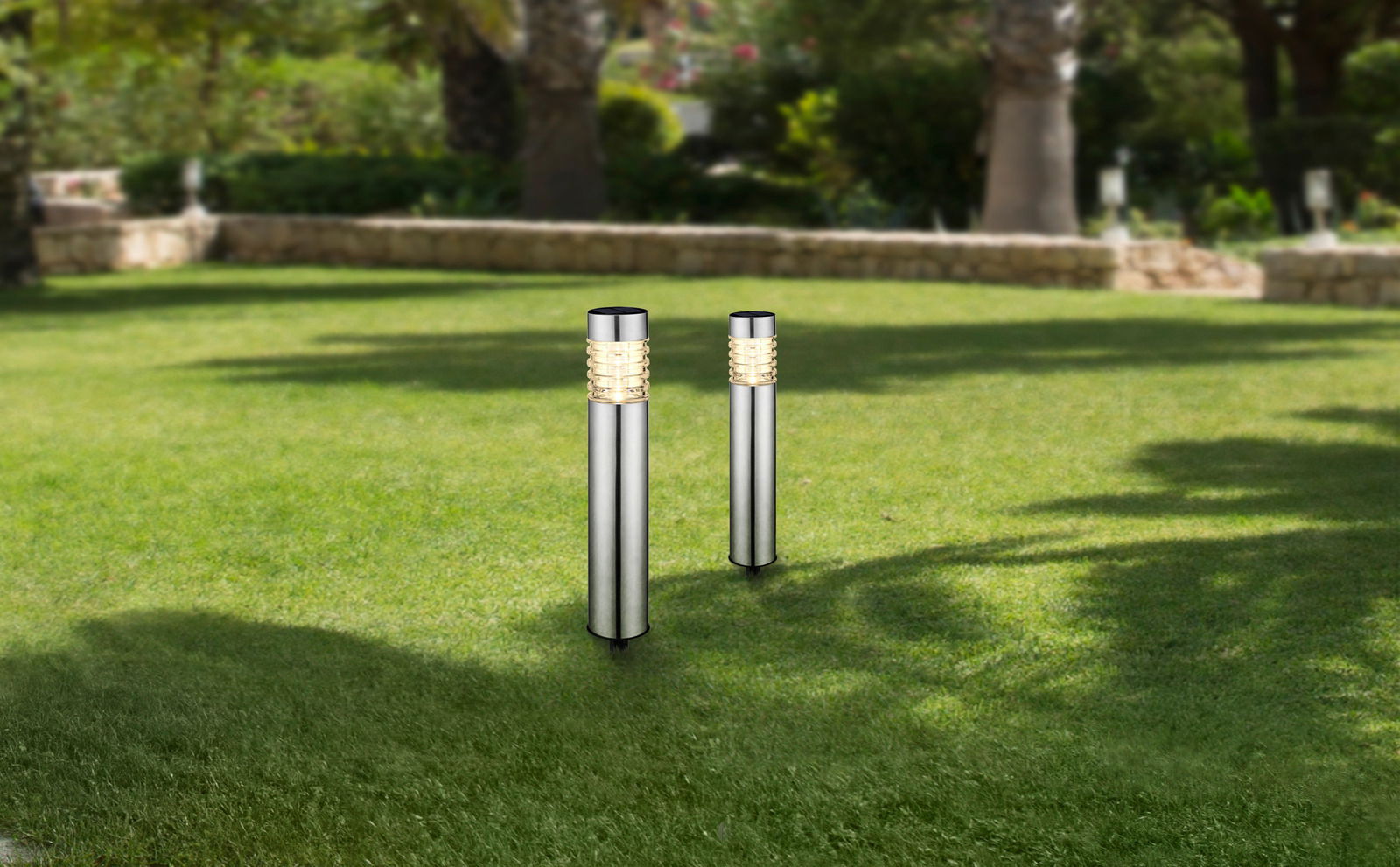 Zwei moderne Solarleuchten aus Edelstahl in einem Garten, seitliche Perspektive.