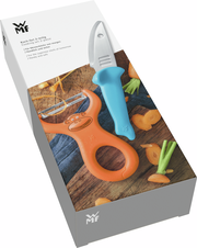 Koch-Set WILLY MIA FRED, bestehend aus einem blauen Messer und einem orangefarbenen Schäler mit Affenmotiv, auf einer Holzoberfläche mit geschnittenen Karotten, aus der Vogelperspektive.