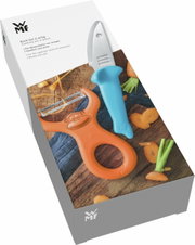 Koch-Set WILLY MIA FRED, bestehend aus einem blauen Messer und einem orangefarbenen Schäler mit Affenmotiv, auf einer Holzoberfläche mit geschnittenen Karotten, aus der Vogelperspektive.