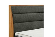 Nahaufnahme eines Boxspringbettes mit grauem, gepolstertem Kopfteil und Holzrahmen, seitliche Perspektive