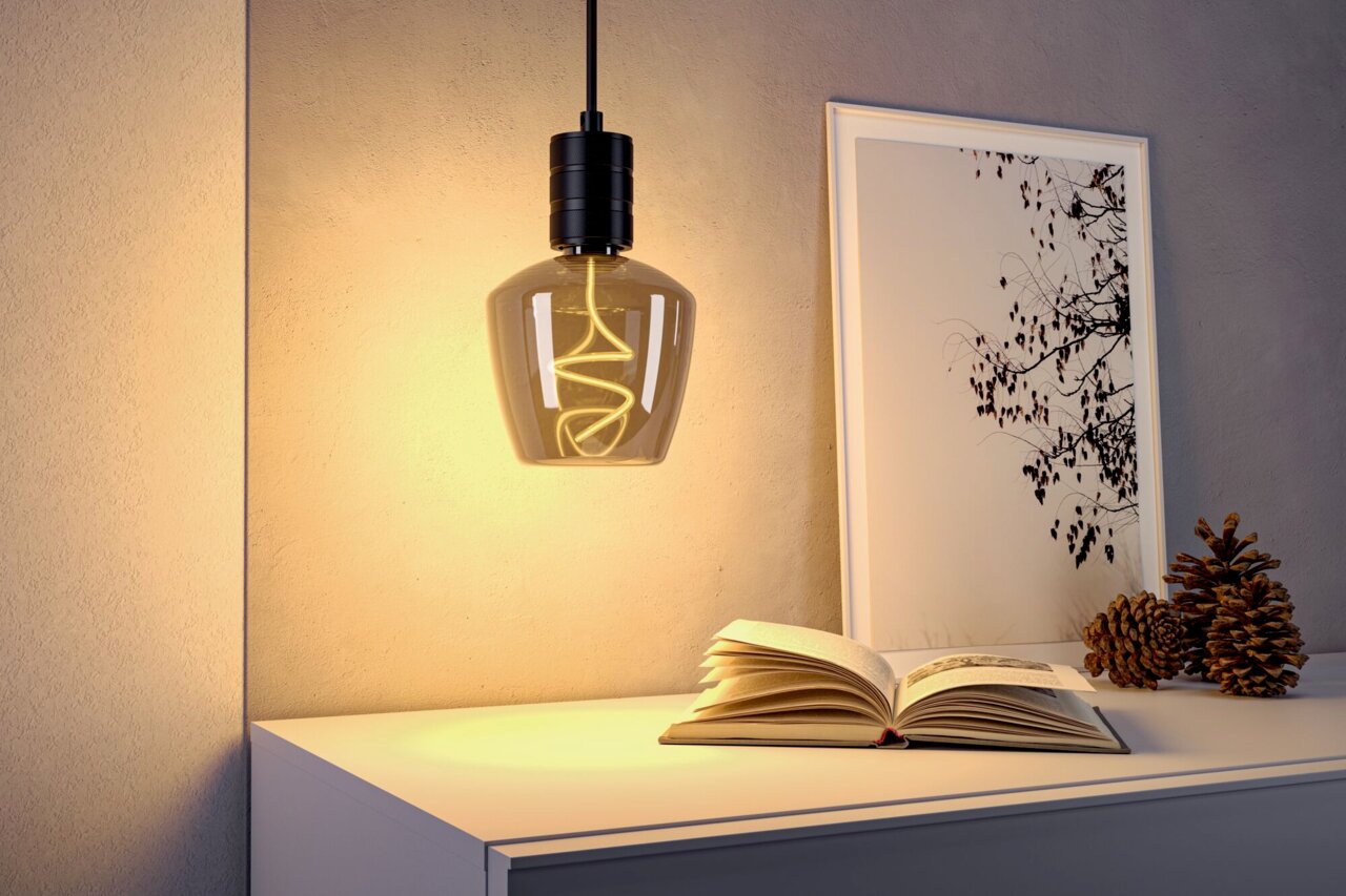LED Leuchtmittel in einer modernen Hängeleuchte, seitliche Perspektive, warmes Licht beleuchtet ein Buch und Dekoration auf einem Tisch.