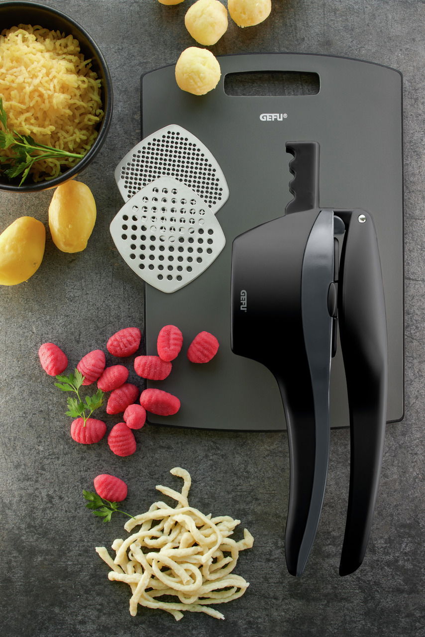 Kartoffel- und Spätzlepresse mit zwei Einsätzen, umgeben von Kartoffeln, Spätzle und Gnocchi, aus der Vogelperspektive.