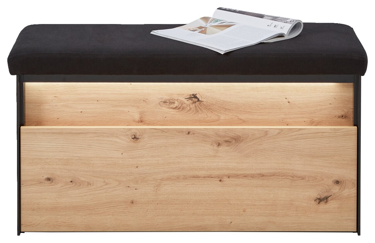 Garderobenbank mit schwarzer Polsterung und Holzfront, frontal fotografiert, mit einer Zeitschrift auf der Sitzfläche.
