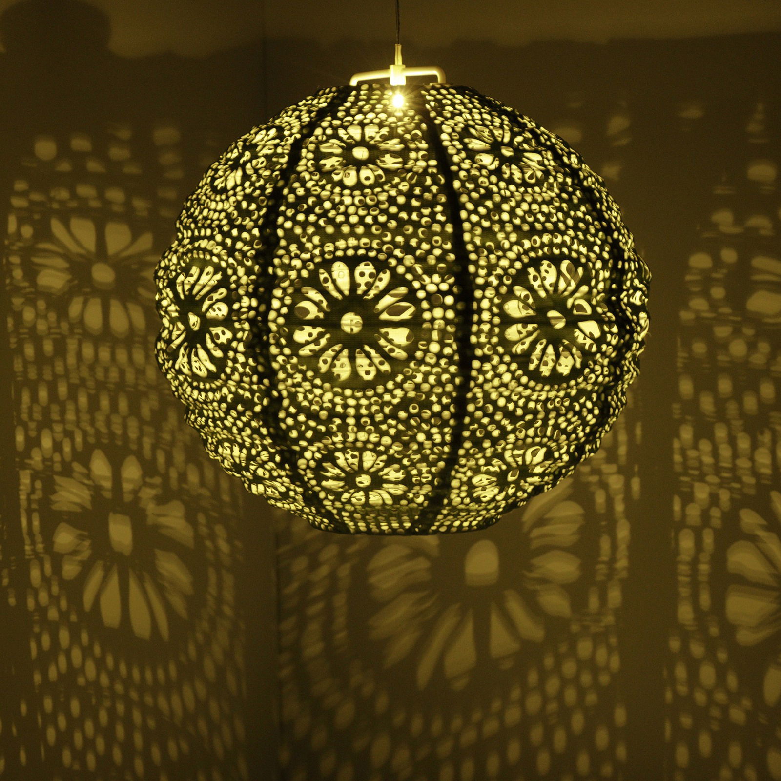 Kugelförmige Solar Laterne mit filigranem Muster, das ein dekoratives Licht- und Schattenspiel an die Wand wirft, seitliche Perspektive