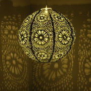 Kugelförmige Solar Laterne mit filigranem Muster, das ein dekoratives Licht- und Schattenspiel an die Wand wirft, seitliche Perspektive