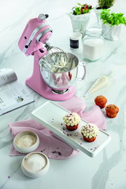 Rosa Küchenmaschine 4.8L Artisan mit Rührbesen, umgeben von Backzutaten und Cupcakes, aus der Vogelperspektive.