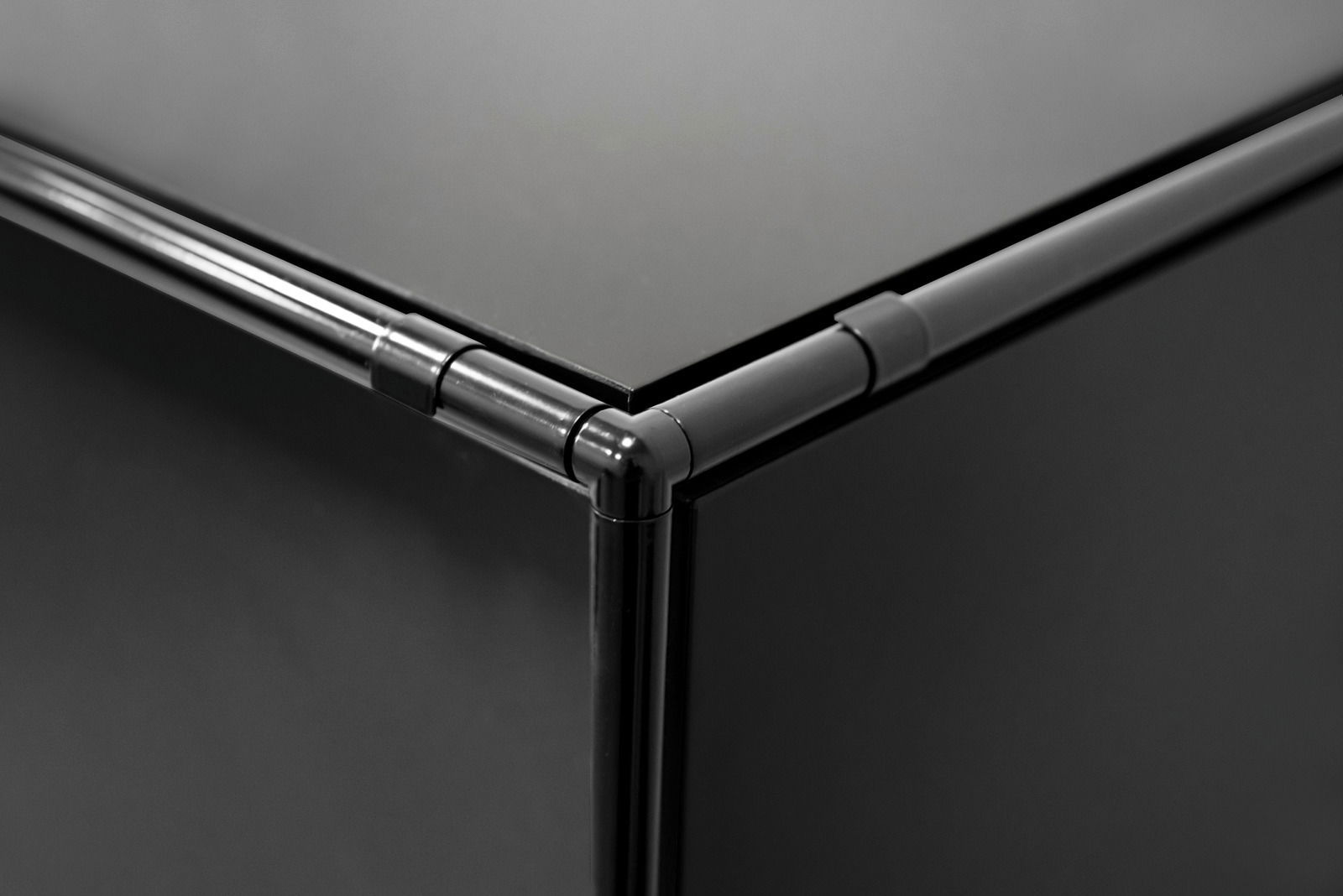 Nahaufnahme einer schwarzen Ecke eines Winkelschreibtisches mit glatten Oberflächen und abgerundeten Kanten, Perspektive von oben.