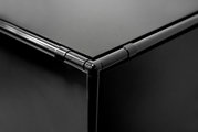 Nahaufnahme einer schwarzen Ecke eines Winkelschreibtisches mit glatten Oberflächen und abgerundeten Kanten, Perspektive von oben.