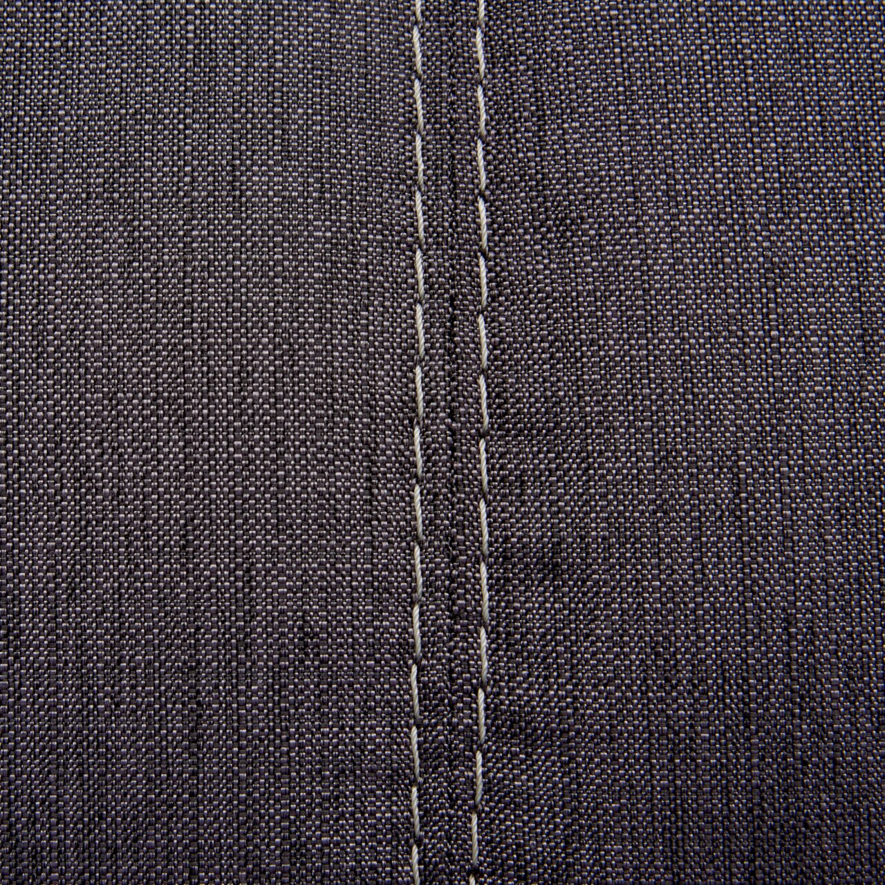 Nahaufnahme einer grauen Stoffoberfläche mit sichtbaren Nähten, perspektivisch von oben betrachtet.