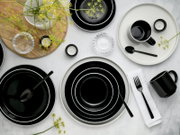 Draufsicht auf ein modernes schwarz-weißes Geschirrset mit Tellern und Schalen, schwarzen Tassen und Besteck, dekoriert mit gelben Blumen auf hellem Untergrund.