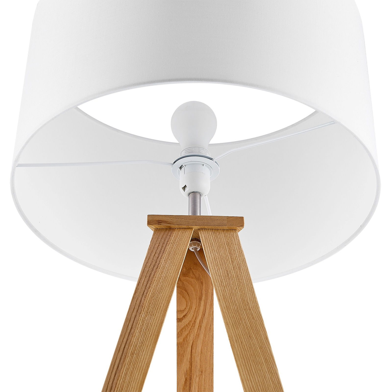 Nahaufnahme einer Stehleuchte mit weißem Lampenschirm und dreibeinigem Holzgestell, von unten betrachtet.