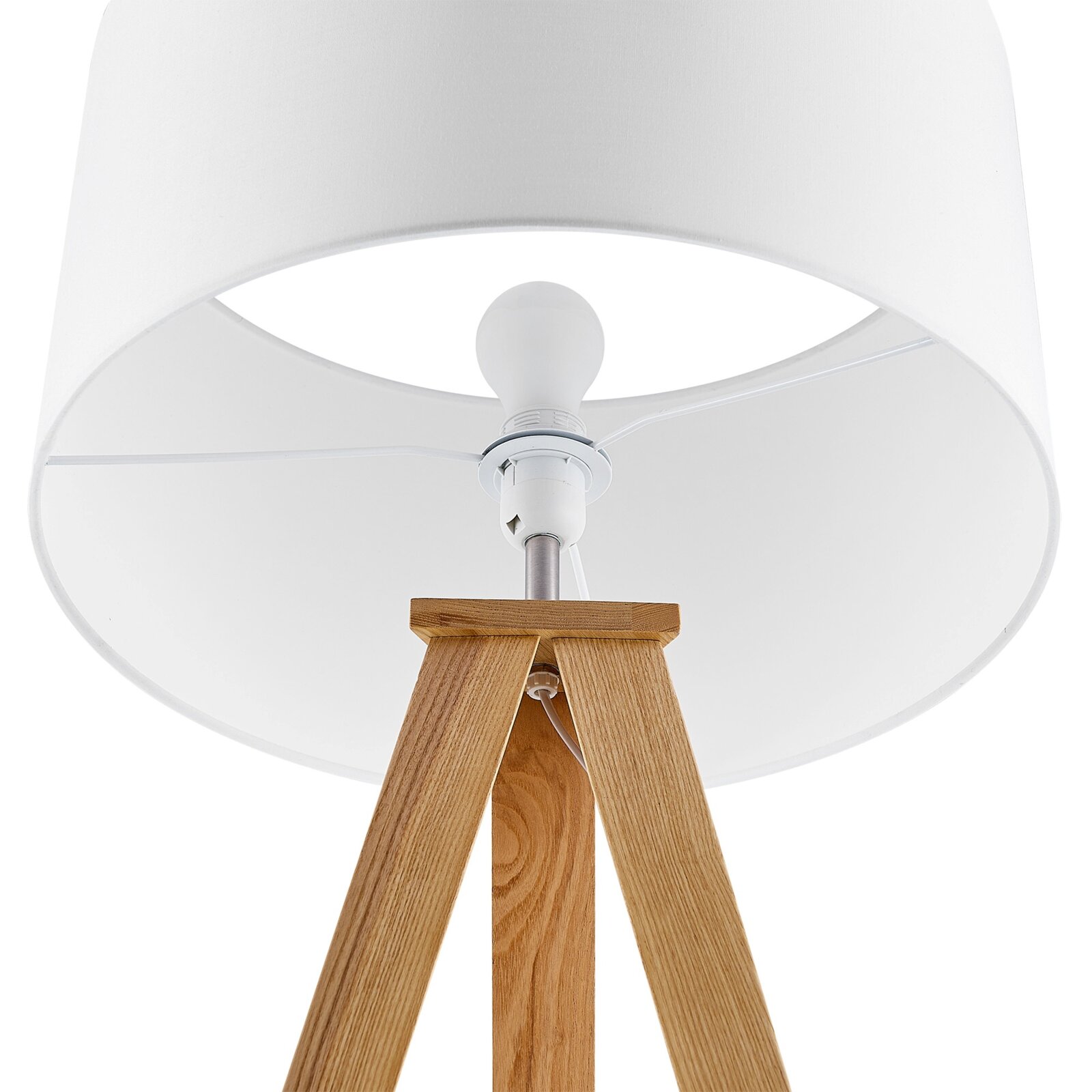 Close-up van een staande lamp met een witte lampenkap en een houten driepoot, gezien van onderaf.