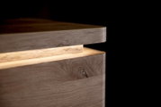 Detailaufnahme in seitlicher Nahperspektive: geöffnete Holzbox mit leicht angehobenem Deckel, sichtbarer Maserung und abgerundeten Kanten vor dunklem Hintergrund