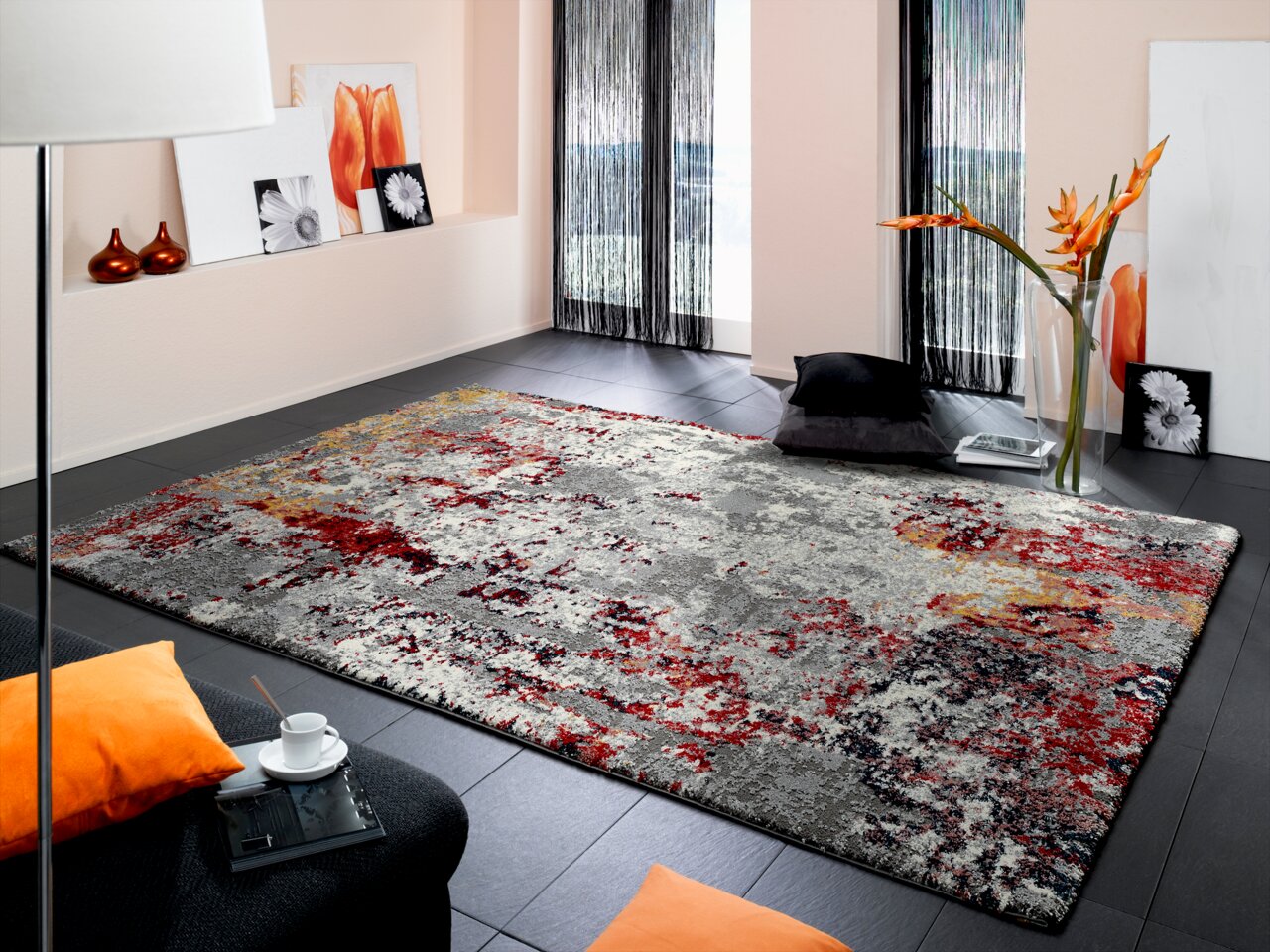 Designer Teppich in einem modernen Wohnzimmer mit abstraktem Muster in Rot-, Grau- und Gelbtönen, aus der Perspektive von schräg oben fotografiert.