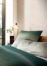 Bettwäsche-Set in Grün- und Weißtönen mit 'bugatti'-Schriftzug, seitliche Perspektive auf das Bett mit dekorativer Beleuchtung und Pflanze im Hintergrund.