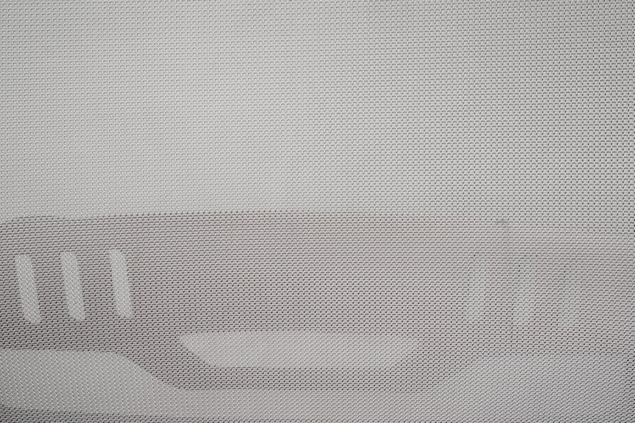 Nahaufnahme eines grauen Netzstoffs mit strukturiertem Muster, vermutlich Teil eines Drehstuhls, von vorne betrachtet.