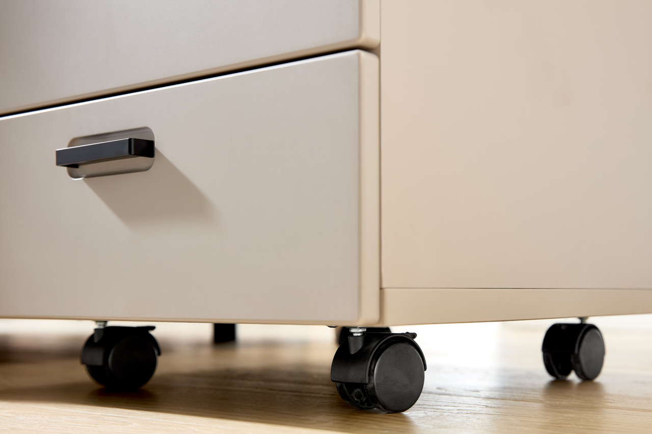 Nahaufnahme eines Rollcontainers mit zwei Schubladen und schwarzen Rollen auf einem Holzboden, seitliche Perspektive.