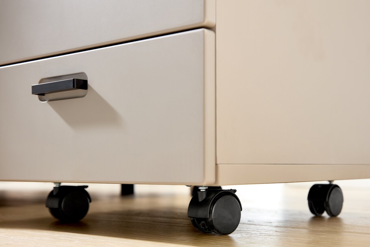 Nahaufnahme eines Rollcontainers mit zwei Schubladen und schwarzen Rollen auf einem Holzboden, seitliche Perspektive.