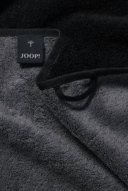 Nahaufnahme eines grauen Handtuchs mit schwarzem Rand und einem Joop-Label.