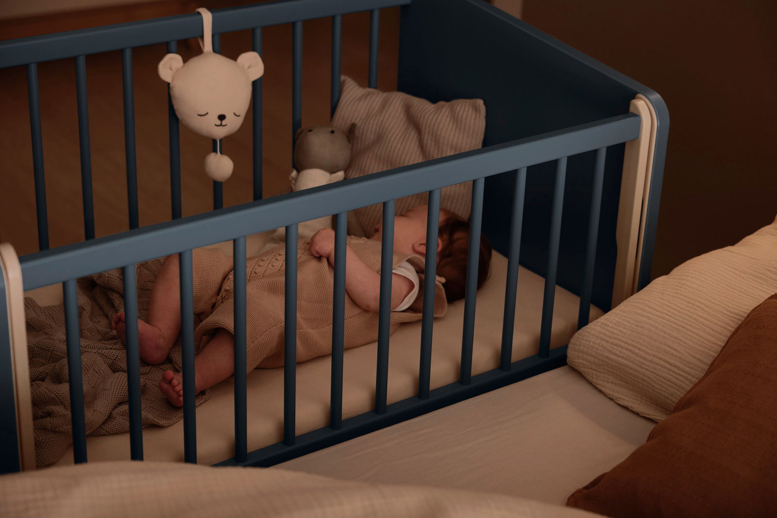 Ein Baby schläft in einem blauen Anstellbett, das an ein größeres Bett angeschlossen ist. Perspektive von oben.