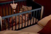 Een baby slaapt in een blauw bijzetbedje dat aan een groter bed is vastgemaakt. Aanzicht van bovenaf.