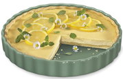 Tortenform mit einem Zitronenkuchen, dekoriert mit Zitronenscheiben und Blüten, aus einer leicht seitlichen Perspektive.