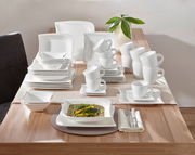 Elegantes weißes Kombiservice La Musica 42-tlg. auf einem Tisch, von oben betrachtet, mit Geschirr, Tassen und Besteck.