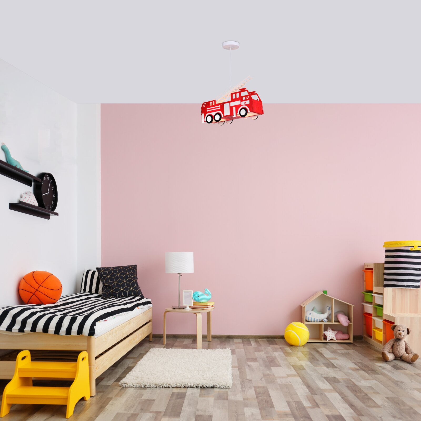Hängeleuchte in Form eines roten Feuerwehrautos, aufgehängt in einem Kinderzimmer mit rosa Wand und Holzboden, aus der Perspektive von vorne betrachtet.