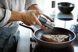 Nahaufnahme einer Person, die ein Steak in einer Stielpfanne PermaDur Advanc 28 auf einem Herd würzt.