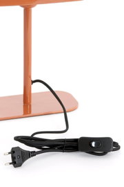 Close-up van een tafellamp in oranje met een zwarte kabel en schakelaar, gezien vanaf de zijkant.