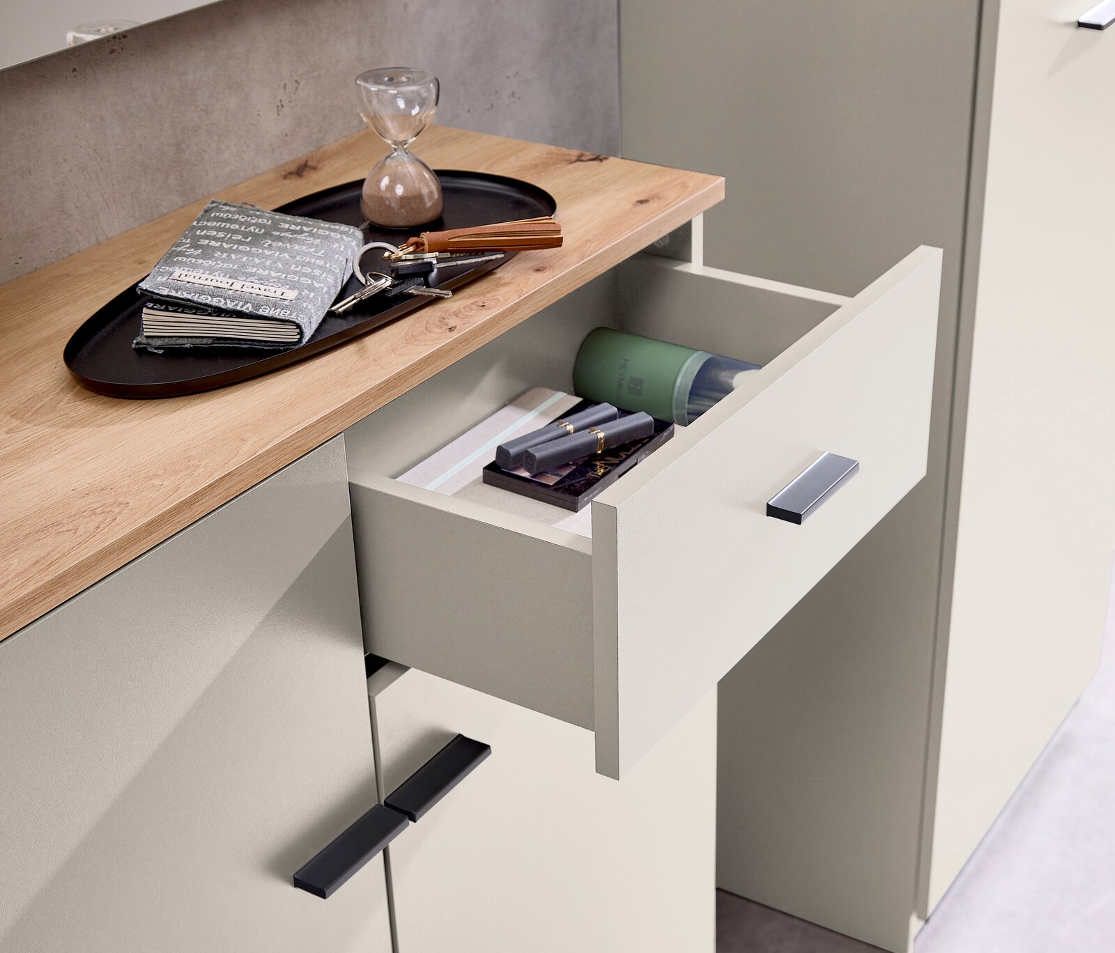 Nahaufnahme einer Kompaktgarderobe mit geöffneter Schublade, die verschiedene Gegenstände enthält, darunter ein Notizbuch, Schlüssel und eine Sanduhr auf der Holzoberfläche.